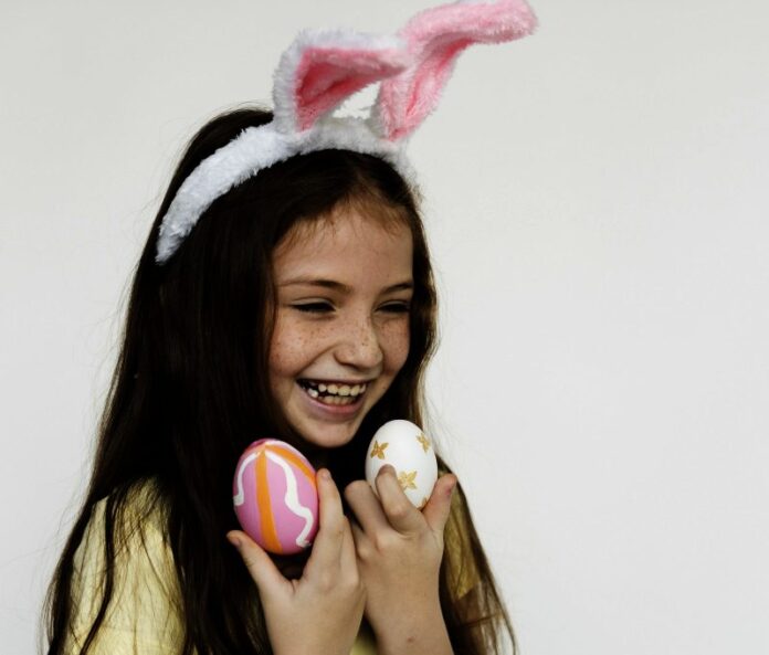 Caucasian girl wearing bunny headband and holding easter eggs with laughing